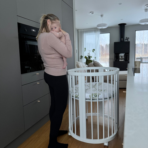 Oran pyöreä pinnasänky Kielo keittiössä renkailla, äiti ja vauva sylissä